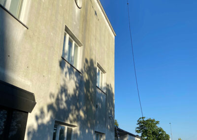 Dron podjetja SANDEX Fly & Clean čisti zgornji del umazane fasade poslovne stavbe.
