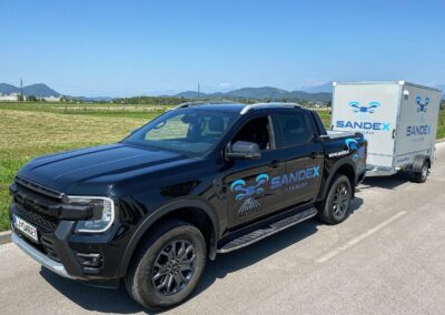 Službeno vozilo in prikolica podjetja SANDEX Fly & Clean, specializiranega za čiščenje s pomočjo dronov v Sloveniji.